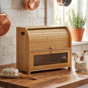 May include: A light brown bamboo bread box featuring a roll-top lid and a lower drawer with a clear glass window. The bread box has a rectangular shape with rounded side panels and small wooden knobs on both the roll-top lid and the drawer front.