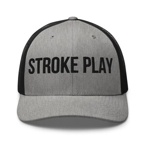 Puede incluir: Gorra de camionero gris con parte trasera de malla negra y visera curva. La parte delantera de la gorra presenta las palabras "STROKE PLAY" en letras mayúsculas negras y en negrita. Cierre a presión.
