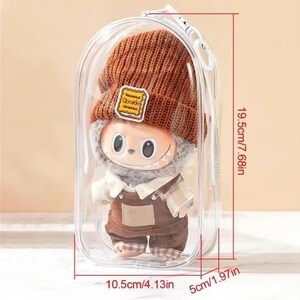 May include: A plush doll in a clear plastic case. The doll is wearing a brown knit hat with a "Cookie" patch, a white scarf, and brown overalls. The case measures 7.68 inches tall, 4.13 inches wide, and 1.97 inches deep.