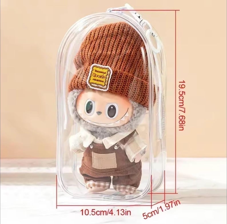 May include: A plush doll in a clear plastic case. The doll is wearing a brown knit hat with a "Cookie" patch, a white scarf, and brown overalls. The case measures 7.68 inches tall, 4.13 inches wide, and 1.97 inches deep.