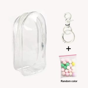May include: A clear, zippered cosmetic bag with a silver-tone keychain and a small bag of colorful pom-poms. The text "Random color" is printed on the bag of pom-poms. The bag is designed to hold makeup or other small items.