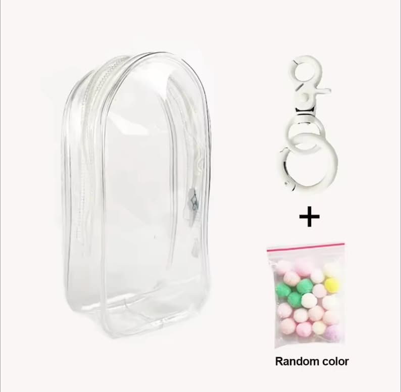 May include: A clear, zippered cosmetic bag with a silver-tone keychain and a small bag of colorful pom-poms. The text "Random color" is printed on the bag of pom-poms. The bag is designed to hold makeup or other small items.