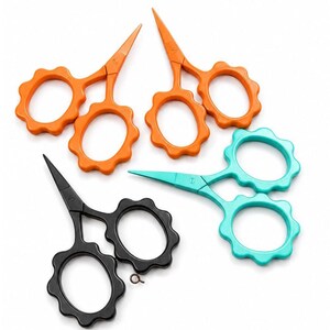Può includere: Quattro paia di forbici piccole con anelli smerlati. Due paia sono arancioni, un paio è color ottanio e un paio è nero. Ogni paio presenta lame metalliche appuntite e una piccola vite nel punto di snodo. Il paio nero include un piccolo anello metallico.