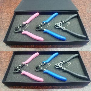 Puede incluir: Un juego de tres pares de alicates para joyería con mangos rosas, azules y negros, presentados en una caja negra con un inserto de espuma. Los alicates están diseñados para la fabricación de joyas.