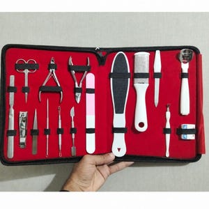 May include: A manicure and pedicure set organized in a black zippered case with a bright red interior lining. The kit includes various stainless steel tools such as nail clippers, cuticle nippers, tweezers, a foot file, and a nail file with pink accents.