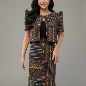 May include: A matching two-piece outfit featuring a patterned jacket and skirt. The jacket has short sleeves and a keyhole neckline. The skirt is a pencil style. The fabric has a mix of colors including brown, green, and red.