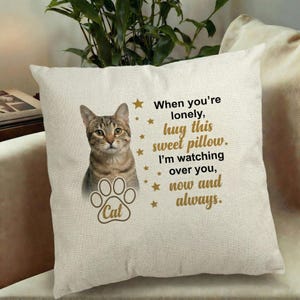 May include: A beige square pillow featuring a tabby cat image and a paw print with the word "Cat". Text reads "When you're lonely, hug this sweet pillow. I'm watching over you, now and always."