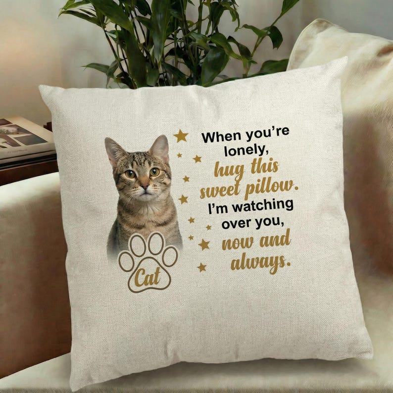 May include: A beige square pillow featuring a tabby cat image and a paw print with the word "Cat". Text reads "When you're lonely, hug this sweet pillow. I'm watching over you, now and always."