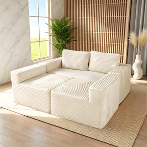 May include: A modular, cream-colored sectional sofa with a corduroy texture. The sofa is composed of several square and rectangular pieces, including armrests and cushions. The sofa sits on a beige rug in a well-lit room with a window and decorative plants.