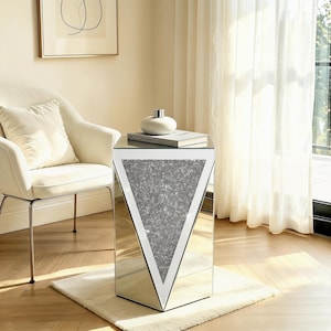May include: A mirrored side table with a triangular, glitter-filled design. The table has a rectangular base and a mirrored top. A white vase and a book rest on top of the table. The table is 20 inches tall.