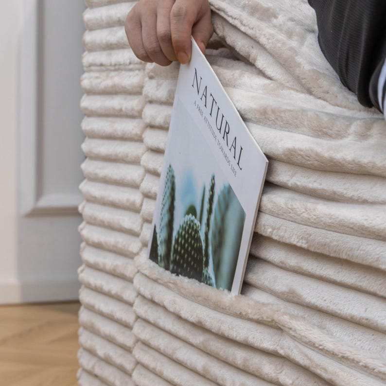 May include: A close-up of a cream-coloured, ribbed fabric with a pocket containing a magazine. The magazine cover displays a cactus image and the word "NATURAL". The fabric has a soft, plush appearance.