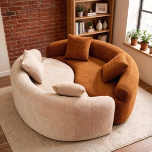 May include: A two-tone curved sofa with matching throw pillows. One section is a light beige, the other is a warm orange-brown. The sofa sits on a patterned rug, with a brick wall and bookshelf in the background.