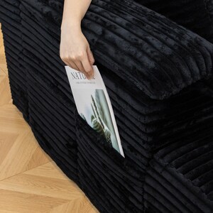 May include: Black corduroy sofa with a pocket. A hand is placing a magazine into the pocket. The magazine has the word "NATURAL" on the cover.