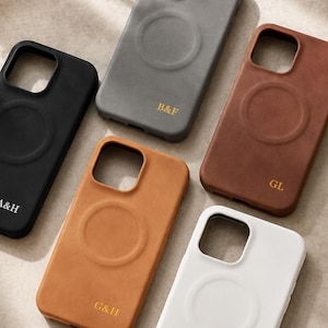 May include: A collection of personalized phone cases in various colors, including black, gray, brown, tan, and white. Each case features a circular design and initials. The cases are arranged on a neutral surface, showcasing a modern aesthetic.