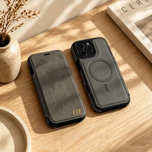 May include: Two dark olive green phone cases for an iPhone. One is a folio-style case with the gold embossed initials GF on the bottom right. The other is a back cover case featuring a circular MagSafe magnetic charging ring and a vertical slot.