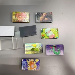 Pu&ograve; includere: Una collezione di magneti rettangolari con varie illustrazioni colorate di personaggi dei cartoni animati, tra cui una creatura simile a una volpe, tre figure marroni, un essere vegetale verde e una creatura elettrica gialla, accanto a cornici in plastica trasparente.