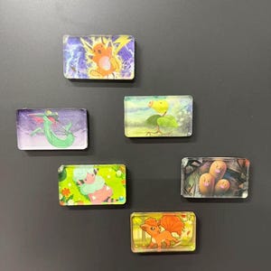 Pu&ograve; includere: Sei magneti rettangolari con illustrazioni colorate di varie creature. I disegni includono una creatura elettrica gialla, una figura serpentina verde, un personaggio vegetale verde, una creatura rosa soffice, tre figure marroni e una creatura arancione simile a una volpe.