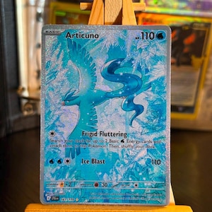 Könnte beinhalten: Eine holografische Articuno-Sammelkarte mit einem blauen Vogel-Pokémon im Flug vor einem verschneiten, eisigen Hintergrund. Die Karte zeigt 110 KP, die Attacken Frigid Fluttering und Ice Blast sowie den Text 161/159 in einer gut lesbaren Schrift.