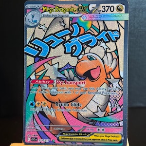 May include: A Mega Dragonite EX Pokémon trading card. The card features an orange and white dragon-like creature with Japanese text. The card has a HP of 370 and includes the abilities "Sky-Transport" and "Ryuno Glide".