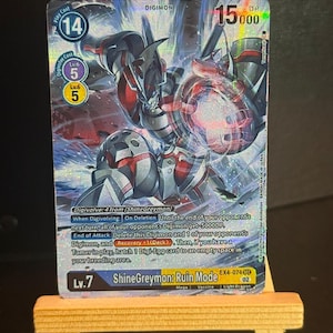 Könnte beinhalten: Eine Digimon-Sammelkarte mit ShineGreymon: Ruin Mode. Die Karte hat ein silbernes, rotes und schwarzes Farbschema mit verschiedenen numerischen Werten und Text. Die Karte wird auf einer kleinen Holzstaffelei präsentiert.