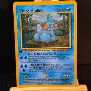 May include: A Pokémon trading card featuring Thicc Mudkip, a blue and orange cartoon character. The card has a swamp scene background and text describing attacks like "Double Mud Plop" and "Tidal Booty Splash".
