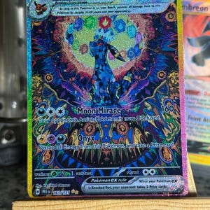Puede incluir: Una carta coleccionable holográfica de Umbreon ex con 280 HP, que presenta una ilustración estilo vitral de la criatura rodeada de gemas coloridas. La carta muestra los ataques Moon Mirage y Onyx, con un borde de lámina de arcoíris.