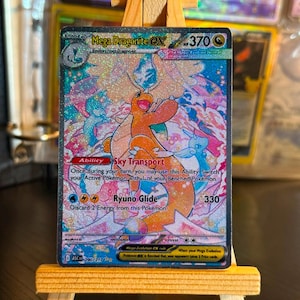 Puede incluir: Una carta coleccionable holográfica Mega Dragonite EX con 370 HP, que muestra un personaje de dragón naranja con alas, ilustraciones de nubes rosas y azules, y el texto Sky Transport y Ryuno Glide impreso en la superficie.