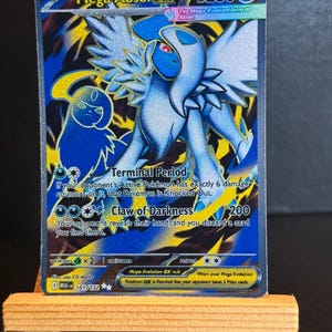 Könnte beinhalten: Eine Mega Absol EX Pokémon-Sammelkarte. Die Karte zeigt ein blau-weißes Wesen mit großen Flügeln und dem Text "Mega Absol EX". Die Karte wird auf einer kleinen Holzstaffelei präsentiert.