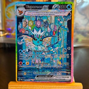 Könnte beinhalten: Eine Vaporeon ex Tera Sammelkarte im Buntglas-Stil mit einem blauen, kristallinen Vaporeon-Charakter. Die Karte zeigt 280 KP, die Attacken Severe Squall und Aquamarine sowie einen regenbogenfarbenen Rand auf einer holografischen Oberfläche.