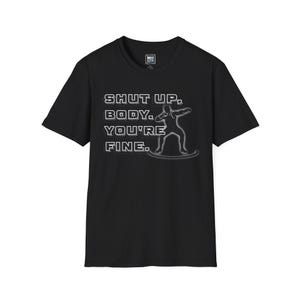 May include: Black t-shirt with the text "SHUT UP, BODY. YOU'RE FINE." in white block letters. A gray outline of a person on a surfboard is next to the text. The shirt has a crew neck and short sleeves.