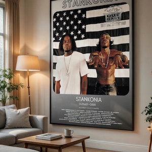 Peut inclure: Affiche encadrée avec deux hommes devant un drapeau américain noir et blanc. L'affiche indique "Stankonia" et "Outkast - 2000". Les hommes portent des t-shirts blancs et des pantalons en cuir.