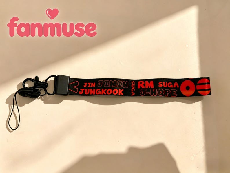 May include: Black lanyard with red text that reads "JIN JIMIN JUNGKOOK RM SUGA J-HOPE". The lanyard has a black clasp and a small black loop. The word "fanmuse" is in pink above the lanyard.