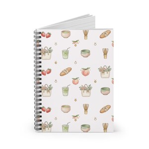 May include: Spiral-bound notebook with a white cover featuring a repeating pattern of strawberries, peaches, matcha bowls, whisk, bread, and tote bags filled with flowers. The notebook is open, revealing lined pages.