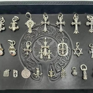 May include: A selection of silver pendants and charms, featuring crosses, stars, and other decorative shapes, presented on a black surface. The pendants vary in size and design, with intricate detailing.