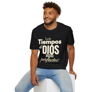 Puede incluir: Camiseta negra con el texto en español "Los Tiempos de DIOS son perfectos" en blanco y dorado. La camiseta es de cuello redondo y la lleva una persona.