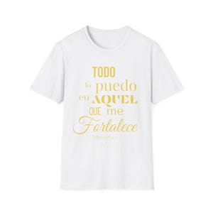 Puede incluir: Camiseta blanca con texto dorado "TODO lo puedo en AQUEL QUE me Fortalece" en una fuente estilizada. El texto está centrado en la parte delantera de la camiseta. La camiseta tiene mangas cortas y cuello redondo.