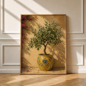 Op de afbeelding: Een ingelijste kunstprint met een citrusboom in een pot met groene bladeren en vruchten in een geel en blauw gedecoreerde keramische plantenbak. De boom staat tegen een getextureerde gouden muur met een klimmende plant met roze bloemen links.