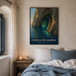 Puede incluir: Una impresión artística enmarcada de Conca dei Marini, Costa Amalfitana, Italia, cuelga sobre una cama. La impresión muestra una cueva marina con una escalera. El texto "CONCA DEI MARINI" y "AMALFI COAST - ITALIA" se muestra en blanco.