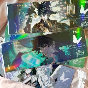 May include: A collection of rectangular bookmarks featuring anime-style illustrations of a character named Amon. The designs include a dark-haired figure in a hat, a raven, a clock face, and a butterfly, with the text The hands that manipulate the passage of time.