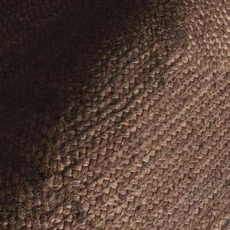 May include: A close-up view of a brown woven textile featuring a dense, interlocking basketweave pattern. The material displays a natural, fibrous texture with variations in light and shadow across the surface, highlighting the thick, sturdy weave.