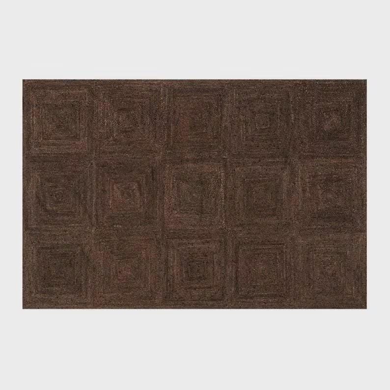 May include: A rectangular area rug featuring a dark brown, monochromatic color palette. The surface is composed of a repeating grid of square sections, each constructed with concentric, spiraling woven patterns that create a textured appearance.