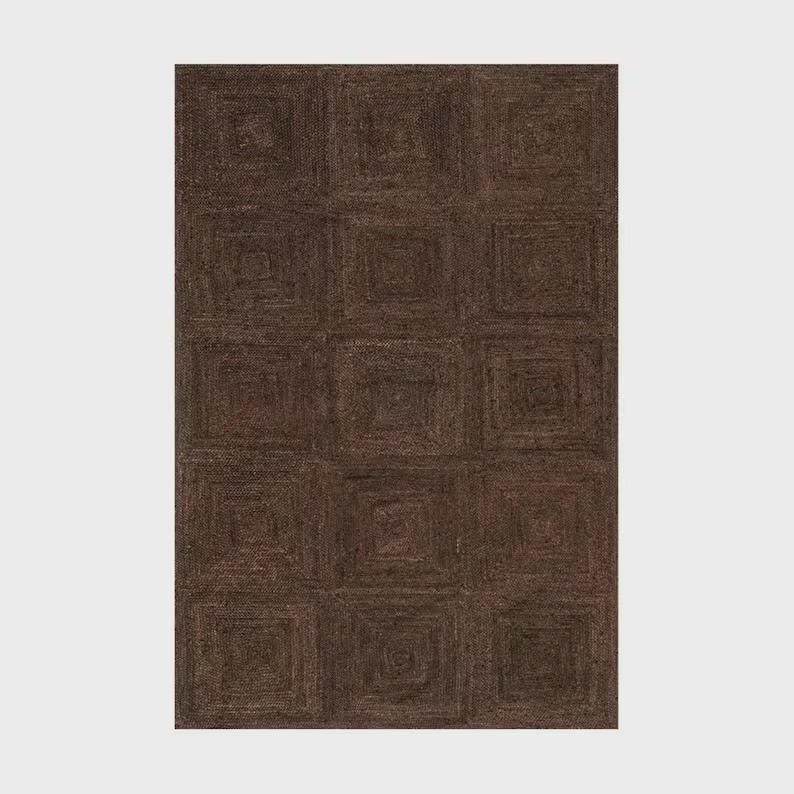 May include: A rectangular area rug in a deep dark brown color featuring a repeating grid pattern of concentric squares. The surface has a textured, woven appearance with visible fiber details throughout the entire construction of the floor covering.