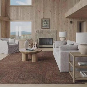 May include: A living room featuring a large brown textured area rug, a light gray sofa, a matching armchair, and a round wooden coffee table with thick cylindrical legs. A wooden side table with shelves sits beside the sofa, and a fireplace is centered.