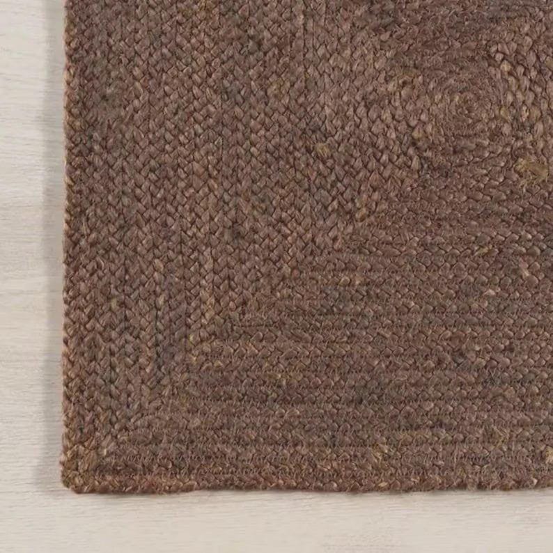 May include: A dark brown rectangular rug featuring a dense, braided texture. The surface is composed of tightly woven natural fibers arranged in a consistent, repeating pattern that creates a uniform, tactile appearance across the entire piece.