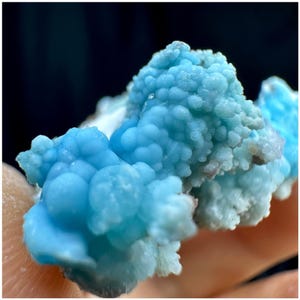 May include: Close-up of a vibrant, light blue mineral specimen. The crystalline structure has a bubbly, clustered appearance, with varying shades of blue and hints of white. The texture appears rough and porous, with a natural, organic aesthetic.
