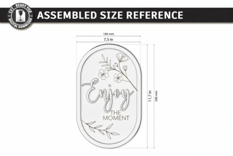Pu&ograve; includere: Un cartello ovale con il testo "Enjoy THE MOMENT" e disegni floreali a linee. Le dimensioni sono 184 mm di larghezza per 298 mm di altezza. Il design include un ramo fiorito nella parte superiore e un ramoscello di foglie in quella inferiore.