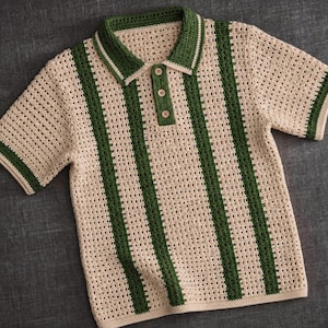 May include: Cream-colored crochet polo shirt with green vertical stripes. The short-sleeved shirt features a collared neckline, three buttons, and green trim on the collar and sleeves. The shirt is made of a breathable, open-weave fabric.