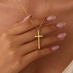 May include: A gold-toned necklace featuring a simple, slender cross pendant suspended from a delicate, fine-link chain. The cross has a smooth, polished finish and a clean, vertical design that hangs centrally from the chain around the neck.