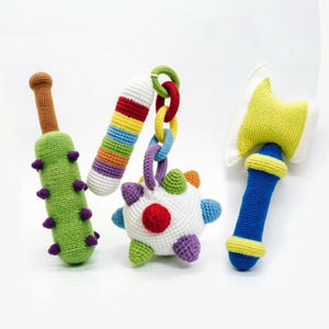 May include: A set of four crocheted toys including a green spiked club with a brown handle, a multi-colored striped cylinder, a white ball with colorful spikes and a chain of rings, and a blue and yellow axe with a white blade edge.