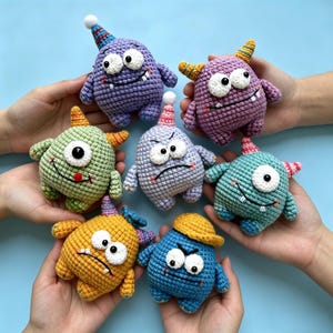 May include: A collection of seven colorful, crocheted monster toys. Each monster has a unique expression, with features like horns, party hats, and one-eyed designs. The toys are in shades of purple, green, yellow, and blue, with white and black accents.